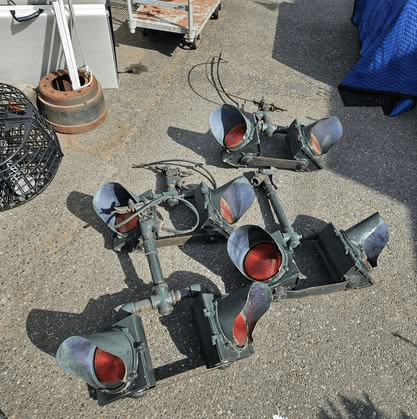 A cluster of old green metal traffic signal housings with red lenses lying on pavement outdoors.