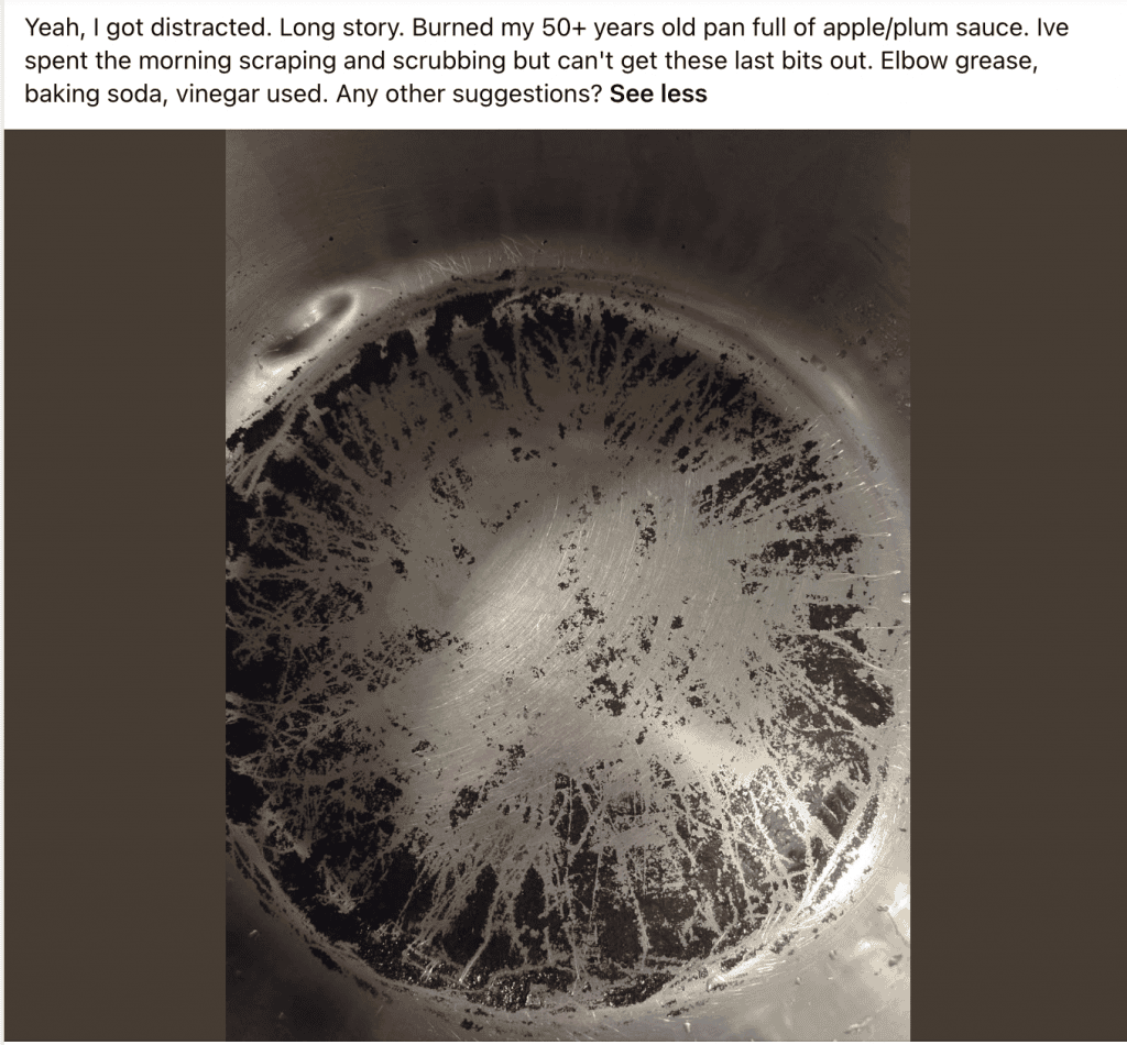 Close-up of a stainless steel pan bottom with extensive black burnt-on residue and scratches across the surface.