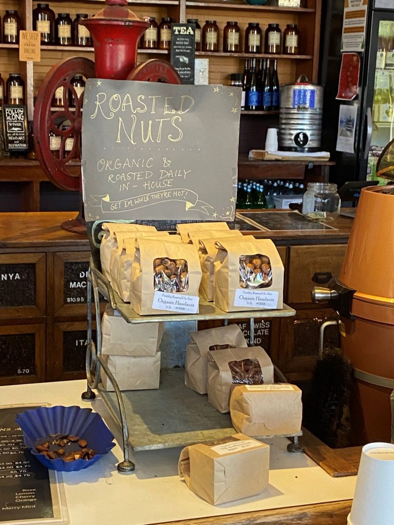 Roasted nuts counter display at the Roasterie | Vashon Maury Island Chalkboard sign reading'Roasted Nuts' advertising organic and daily-in-house roasting on a shop counter with bags of nuts nearby.