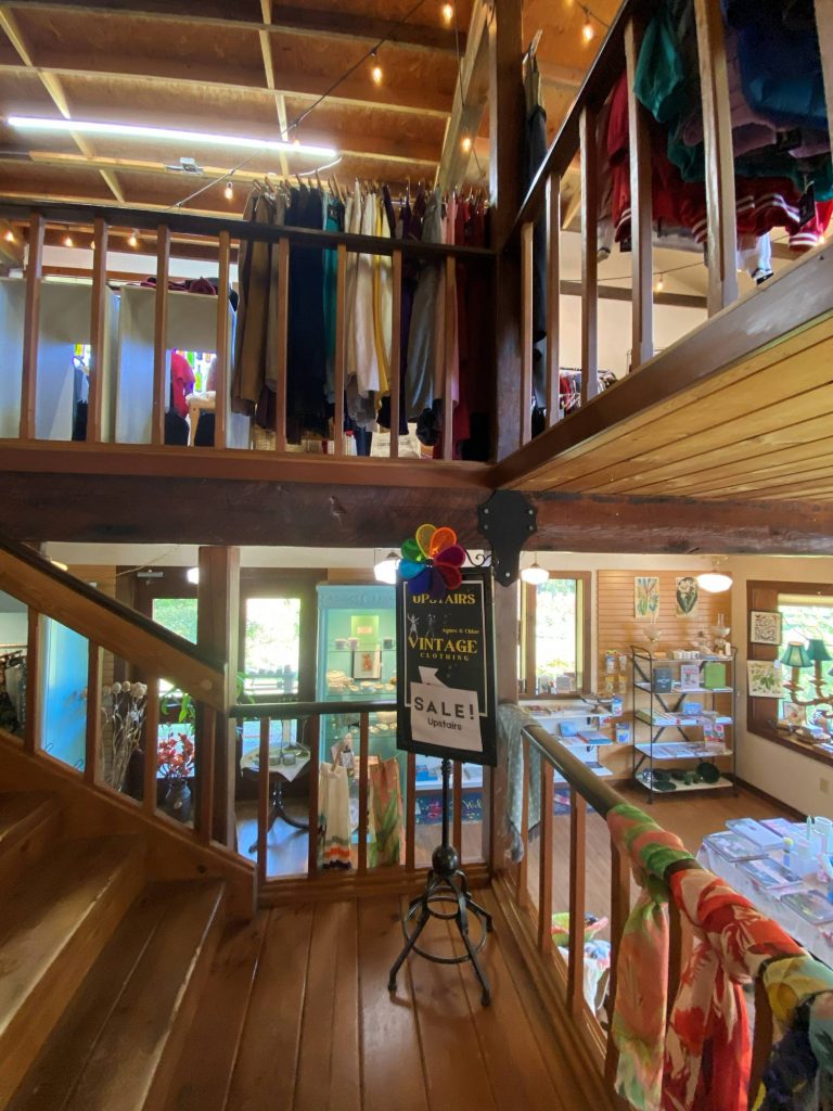 Find vintage delights upstairs | Vashon Maury Island Clothing shop interior with shirts hanging on racks along a wooden mezzanine and a stair railing in the foreground.